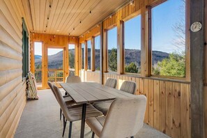 A wooden cabin with a dining area, large windows, and a view of the mountains. - Snow Cap w/ Hot Tub and Fireplace! (Bethel)