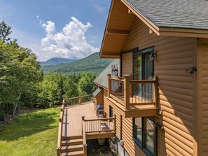 A log cabin with a balcony, a deck, and a view of a mountain range.