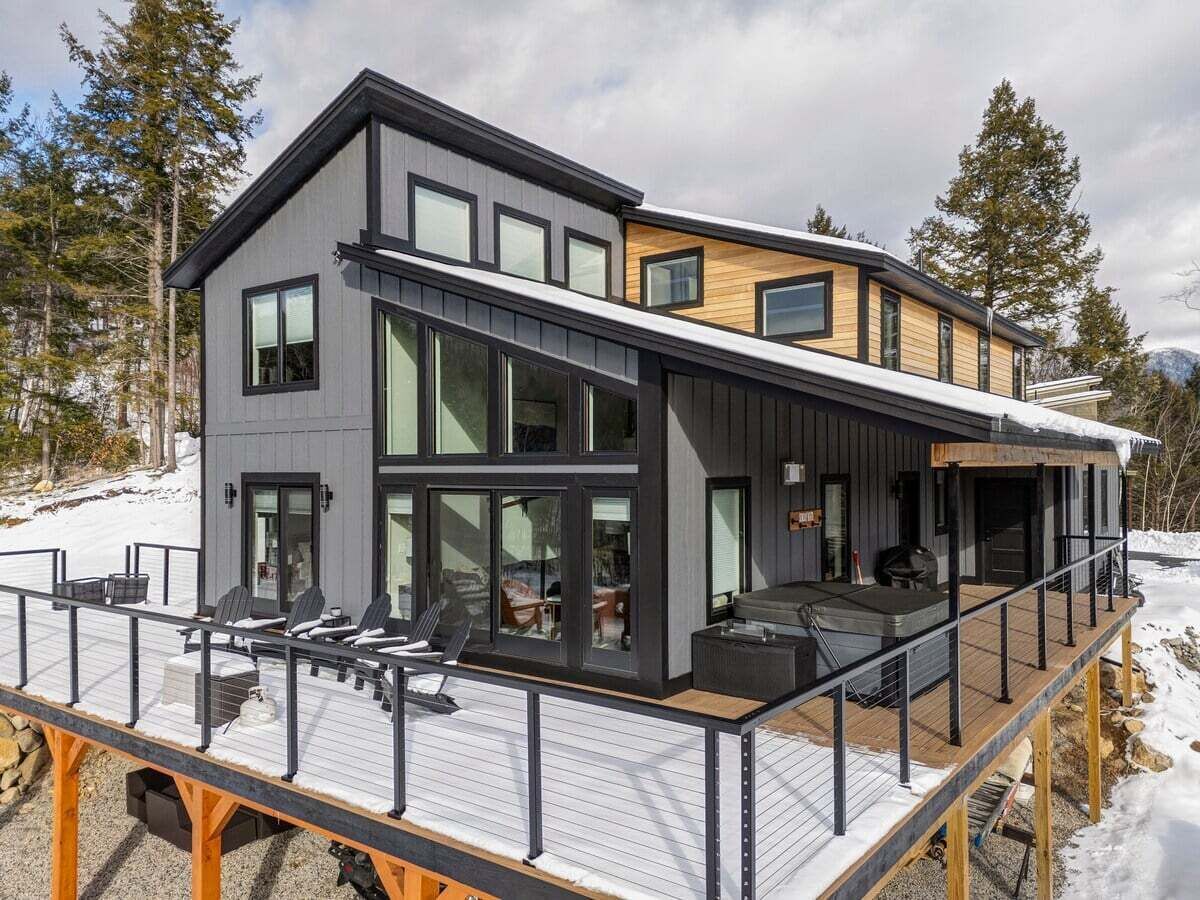 Et moderne hus med to etager, en terrasse, store vinduer og et overdækket udendørs siddeområde.