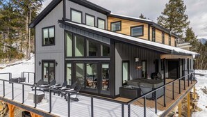 Ein modernes, zweistöckiges Haus mit einer Terrasse, großen Fenstern und einem überdachten Sitzbereich im Freien.