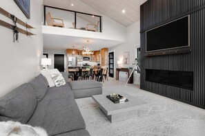 A modern living room with a sectional sofa, a coffee table, and a large flat-screen TV mounted on a dark wall.