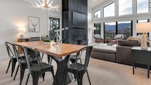 Ein modernes Wohnzimmer mit Essbereich, Kamin und großen Fenstern mit Blick auf die Berge.