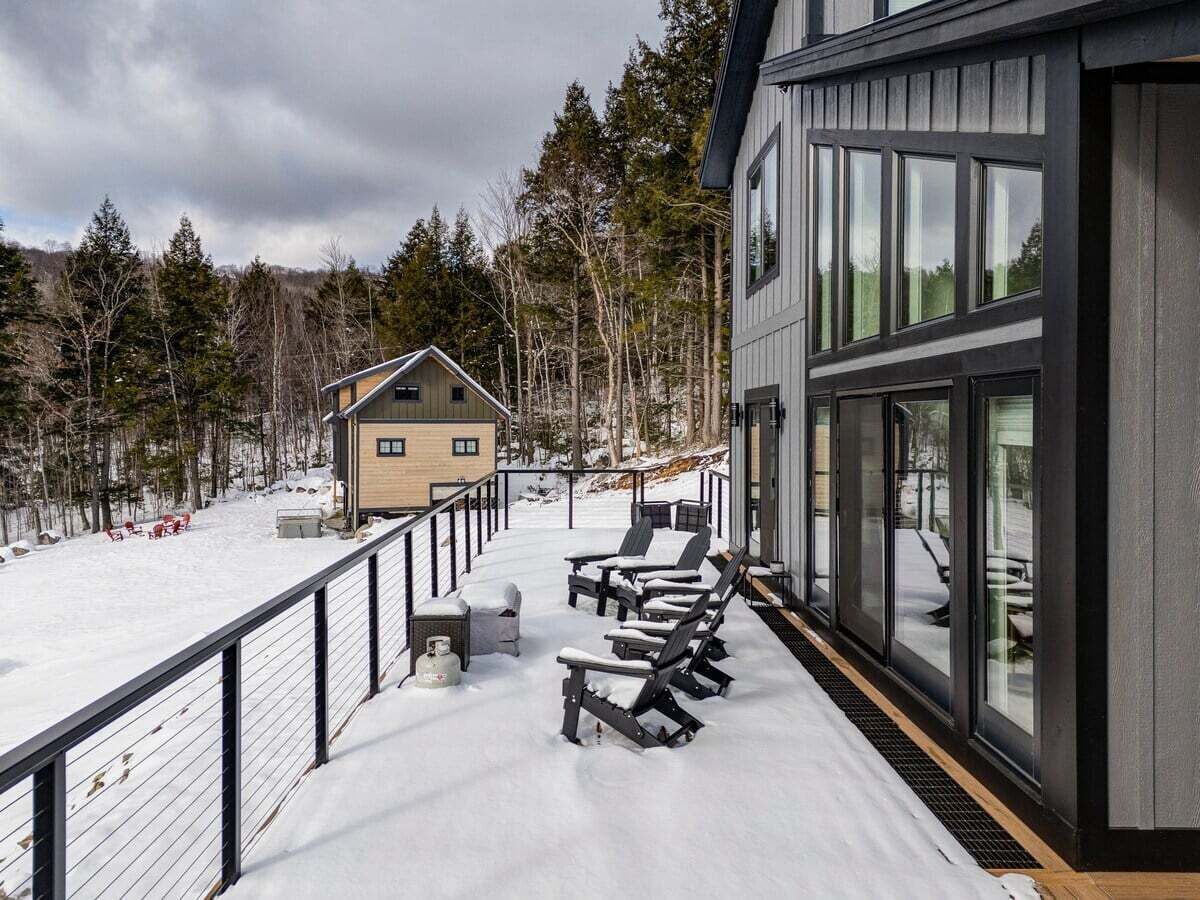 A snow-covered deck with lounge chairs and a small building in the background.