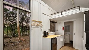 Eine kleine Küche mit Holzarbeitsplatte, Spüle und Geschirrspüler. Draußen befindet sich eine Holzterrasse mit Tisch und Stühlen.