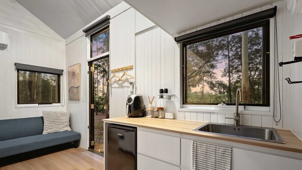 Eine kleine Küche mit eingebautem Geschirrspüler, einer Holz Arbeitsplatte und einem großen Fenster mit Blick auf Bäume.