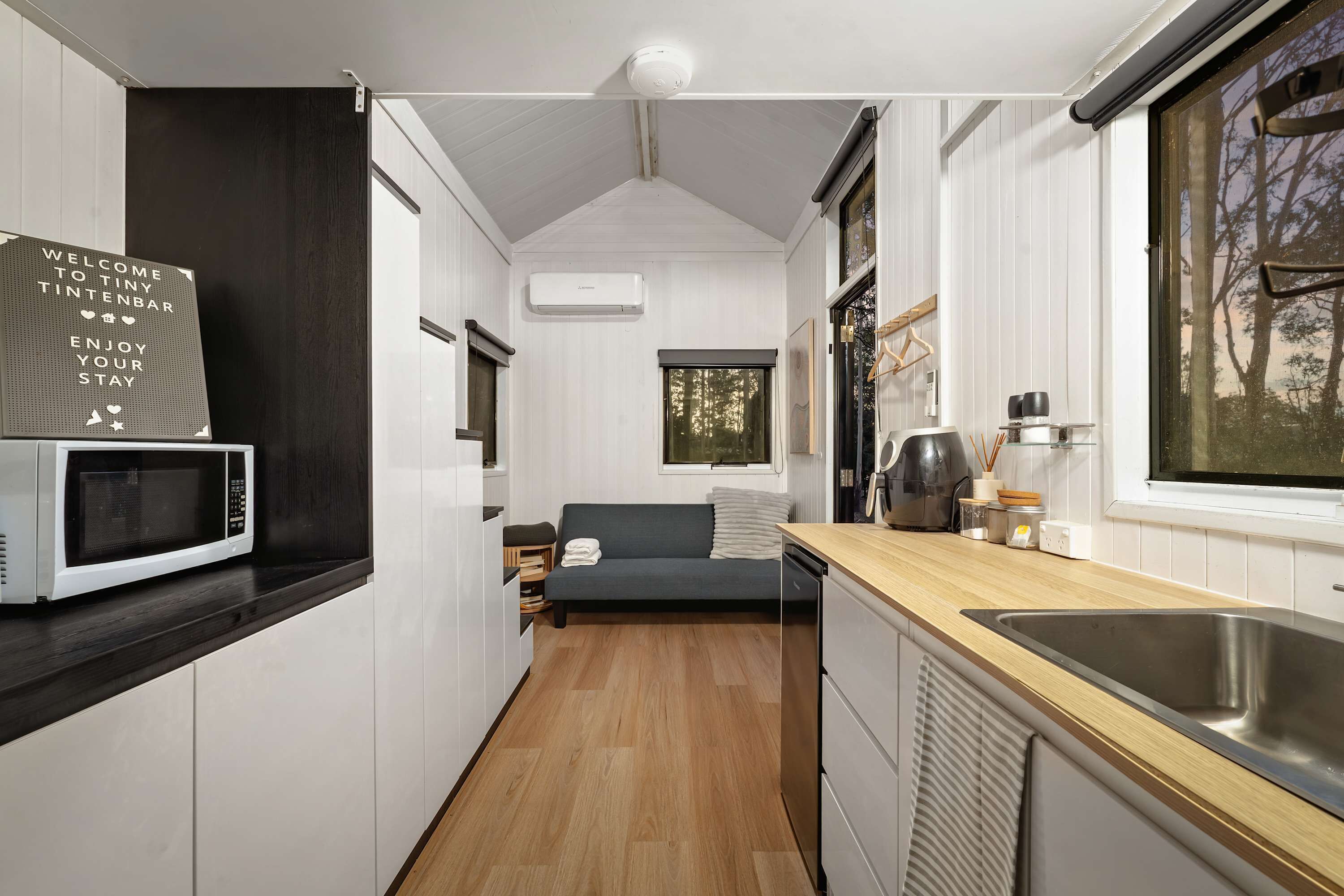 Cocina compacta con microondas, un lavamanos y ventana con vistas a un bosque.
