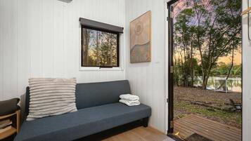 A room with a grey sofa, a window, and a view of a lake and trees.
