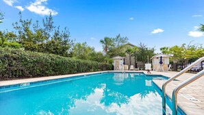 A clear blue swimming pool with a metal ladder, surrounded by greenery and two small structures. - Pond-Side Retreat | Pool | Bikes | Beach Chairs & Wagon | Patio w/ Grill | Clean & Bright End Unit (St. Simons Island)