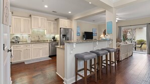 A spacious kitchen with white cabinetry, a central island with bar stools, and a dining area with a view to the outdoors. - Pond-Side Retreat | Pool | Bikes | Beach Chairs & Wagon | Patio w/ Grill | Clean & Bright End Unit (St. Simons Island)