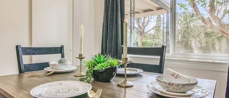 Una mesa de comedor dispuesta con platos, cubiertos, velas y una planta en maceta.