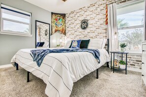A bedroom with a brick wall, a bed with a white and blue bedspread, a window, and a wall-mounted tapestry.