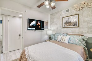 A bedroom with a bed, a television mounted on the wall, and a ceiling fan.