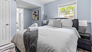 Une chambre à coucher avec un lit, des tables de chevet, une fenêtre et une porte.