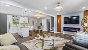 Un salon moderne avec une cheminée, un coin repas et une cuisine en arrière-plan.