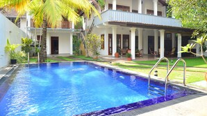 A swimming pool with a clear blue water surface, surrounded by a well-maintained lawn and palm trees. - Surf Villa (Hikkaduwa)