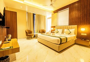 Habitación de hotel con una cama grande, un escritorio con computadora, una silla, un televisor y una ventana con cortinas.