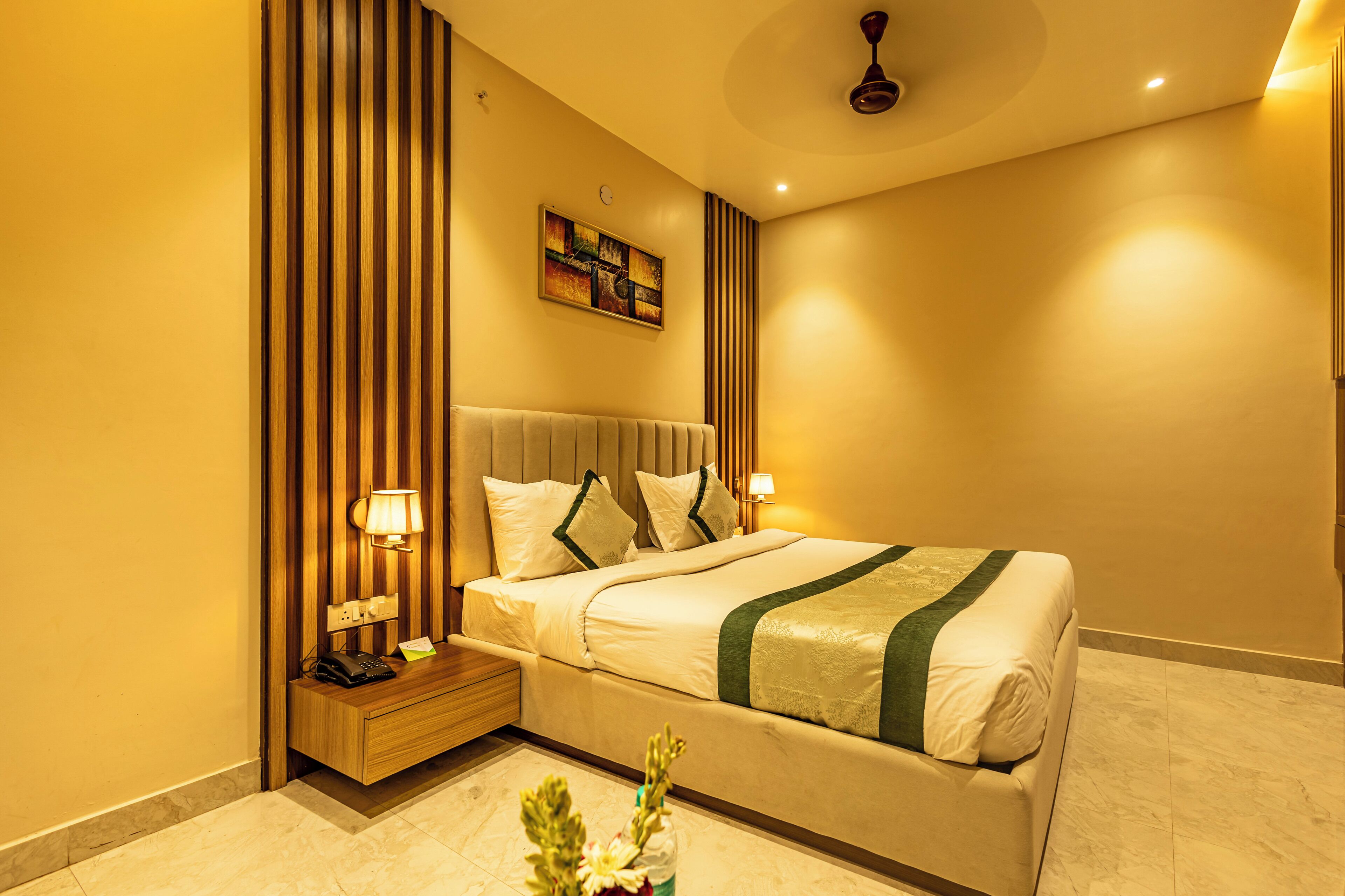 A hotel room with a bed, bedside lamps, a nightstand, a wall clock, and a ceiling fan.