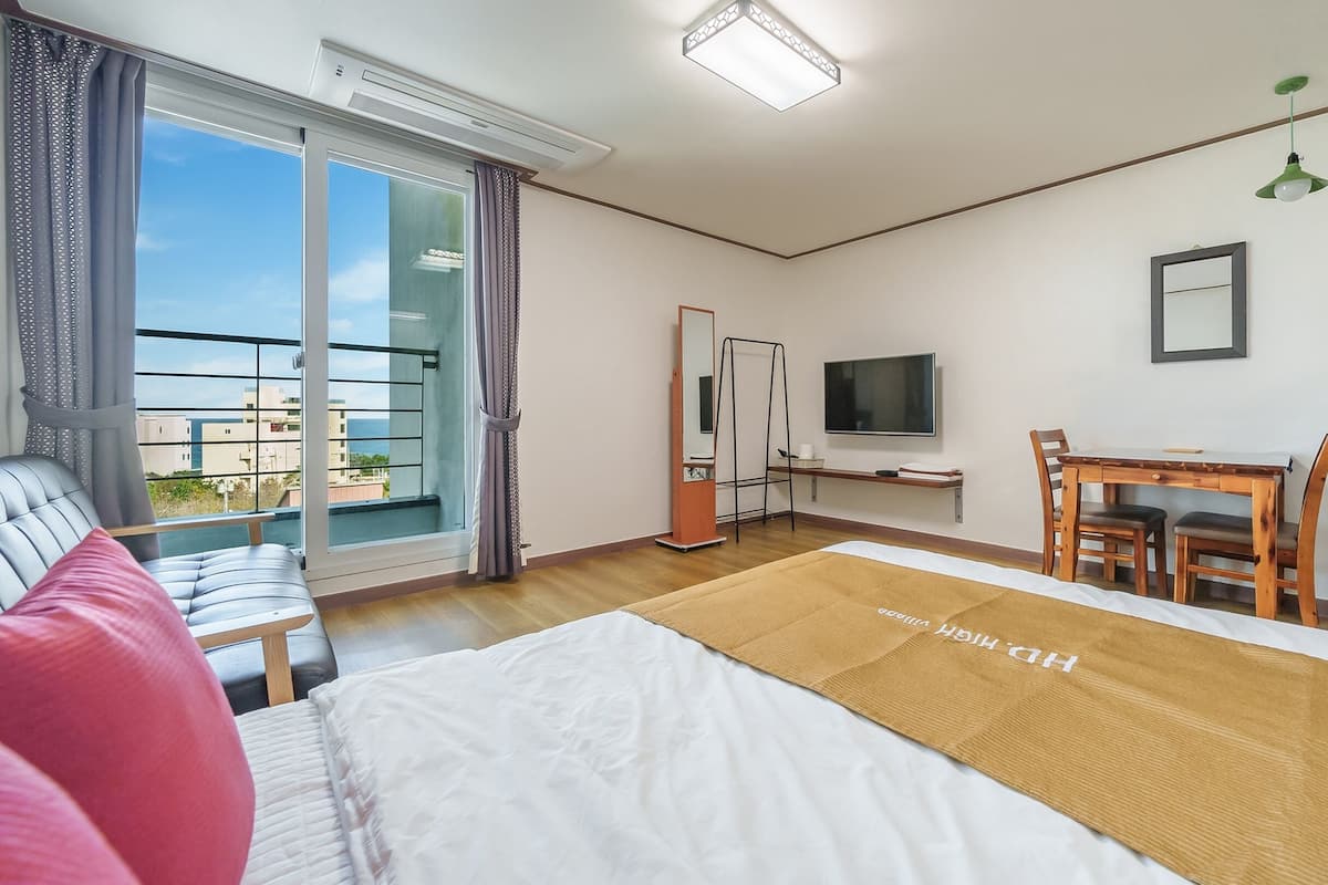 Een hotelkamer met een bed, een bureau met stoel, een televisie en een balkon met uitzicht op gebouwen.