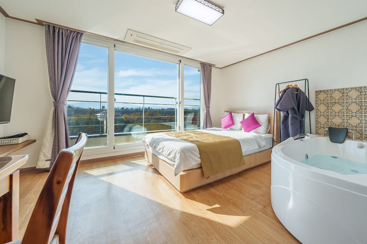 Een moderne hotelkamer met een groot bed, een zithoek met een fauteuil, een bureau, een televisie en een ruime badkuip.