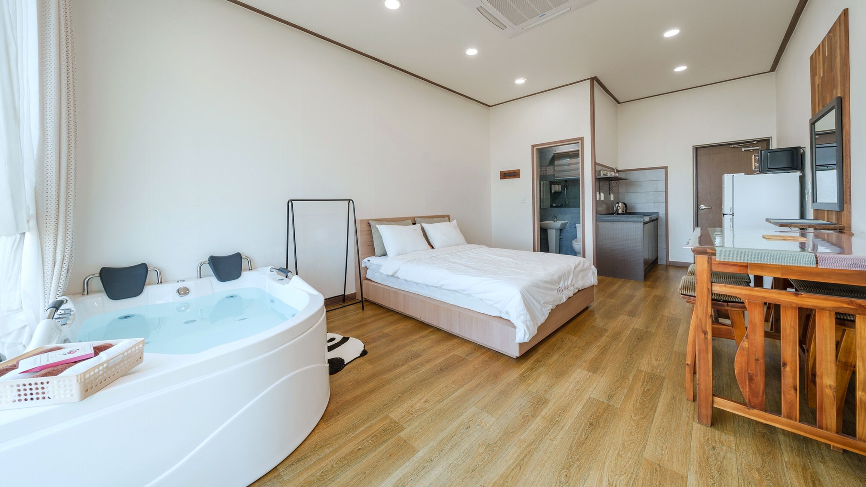 Ein Schlafzimmer mit einer großen Badewanne, einem Bett, einem Holztisch und einer kleinen Küchenzeile.