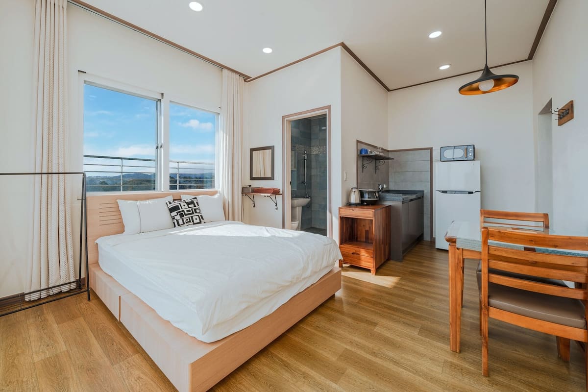 Een moderne slaapkamer met een groot bed, een houten bureau, een stoel, een kleine kitchenette en een badkamer.