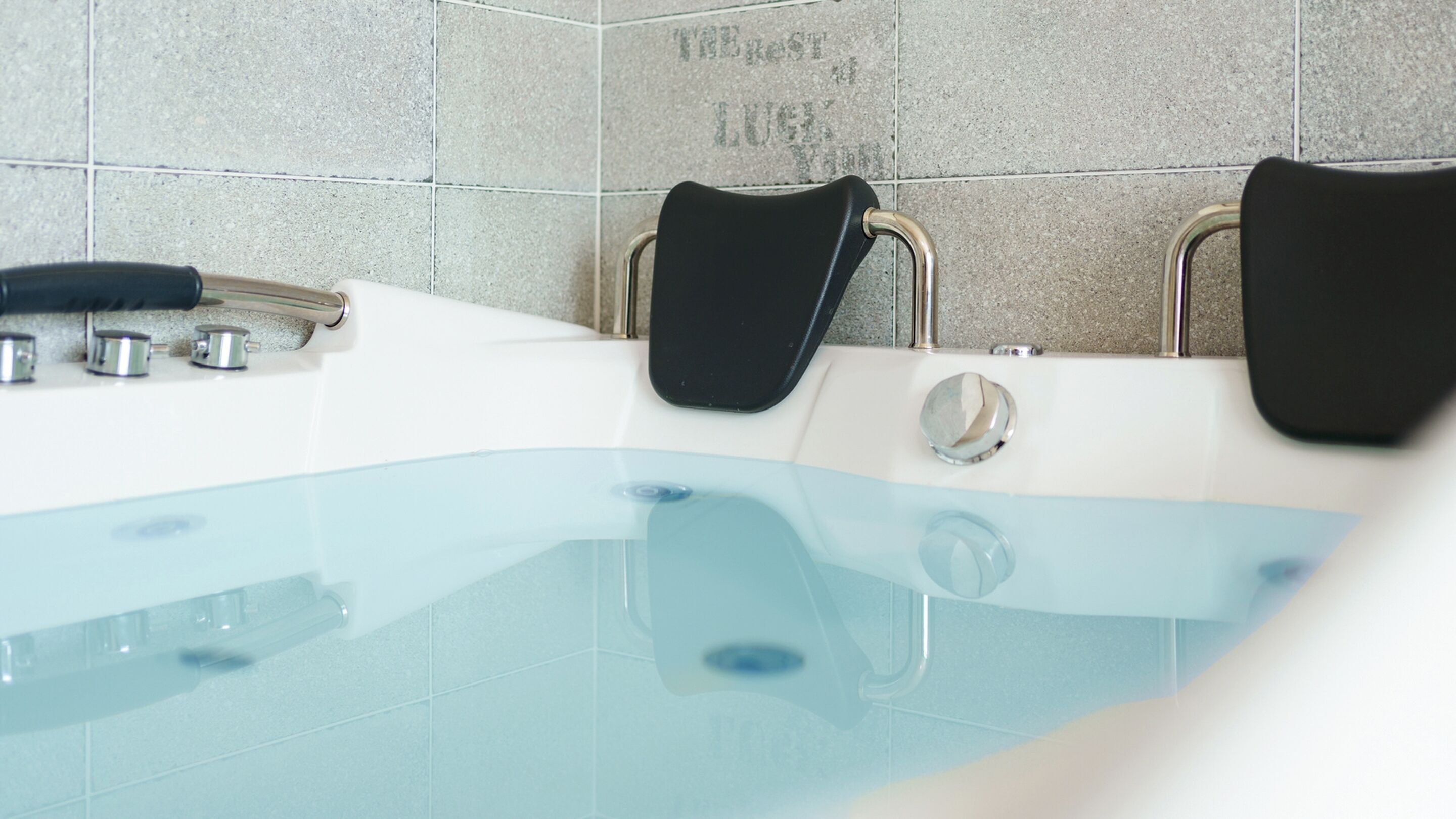 A modern bathroom with a glass-enclosed hot tub, chrome fixtures, and a tiled wall with a motivational quote.