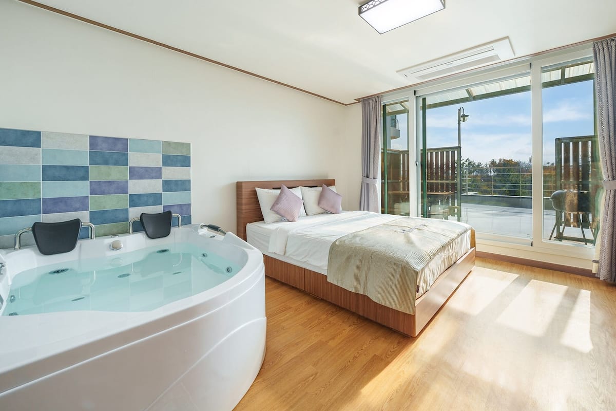 Een moderne slaapkamer met een groot bed, een aparte badkamer met een jacuzzi, en een balkon met uitzicht.