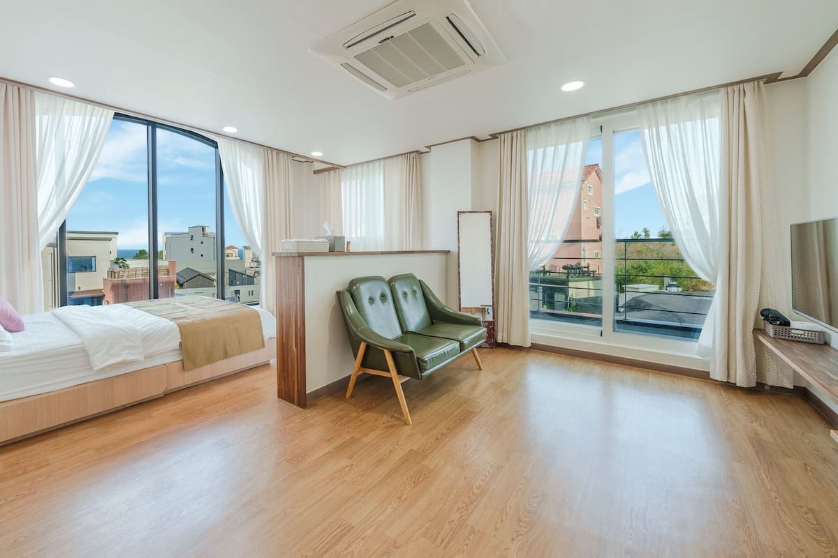 Een moderne hotelkamer met een bed, een groene bank en grote ramen met uitzicht over de stad.