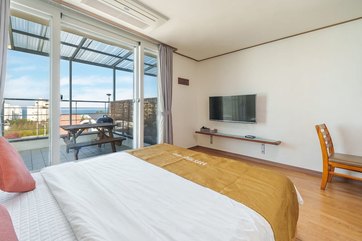 Hotelkamer met een bed, een aan de muur bevestigde televisie, een houten stoel en een balkon met tafel en barbecue.