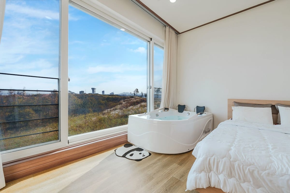 Een moderne slaapkamer met een groot raam, een badkuip en een bed.