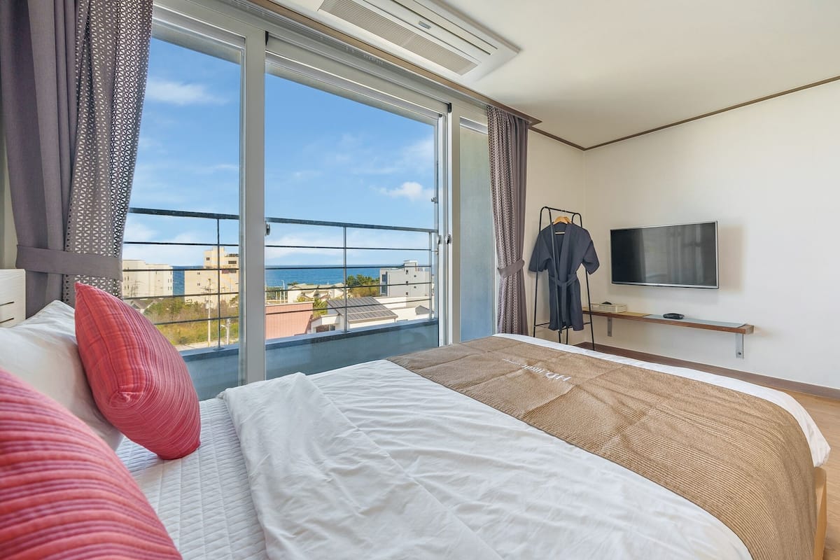 Een hotelkamer met een groot bed, een televisie, een bureau en uitzicht op zee.