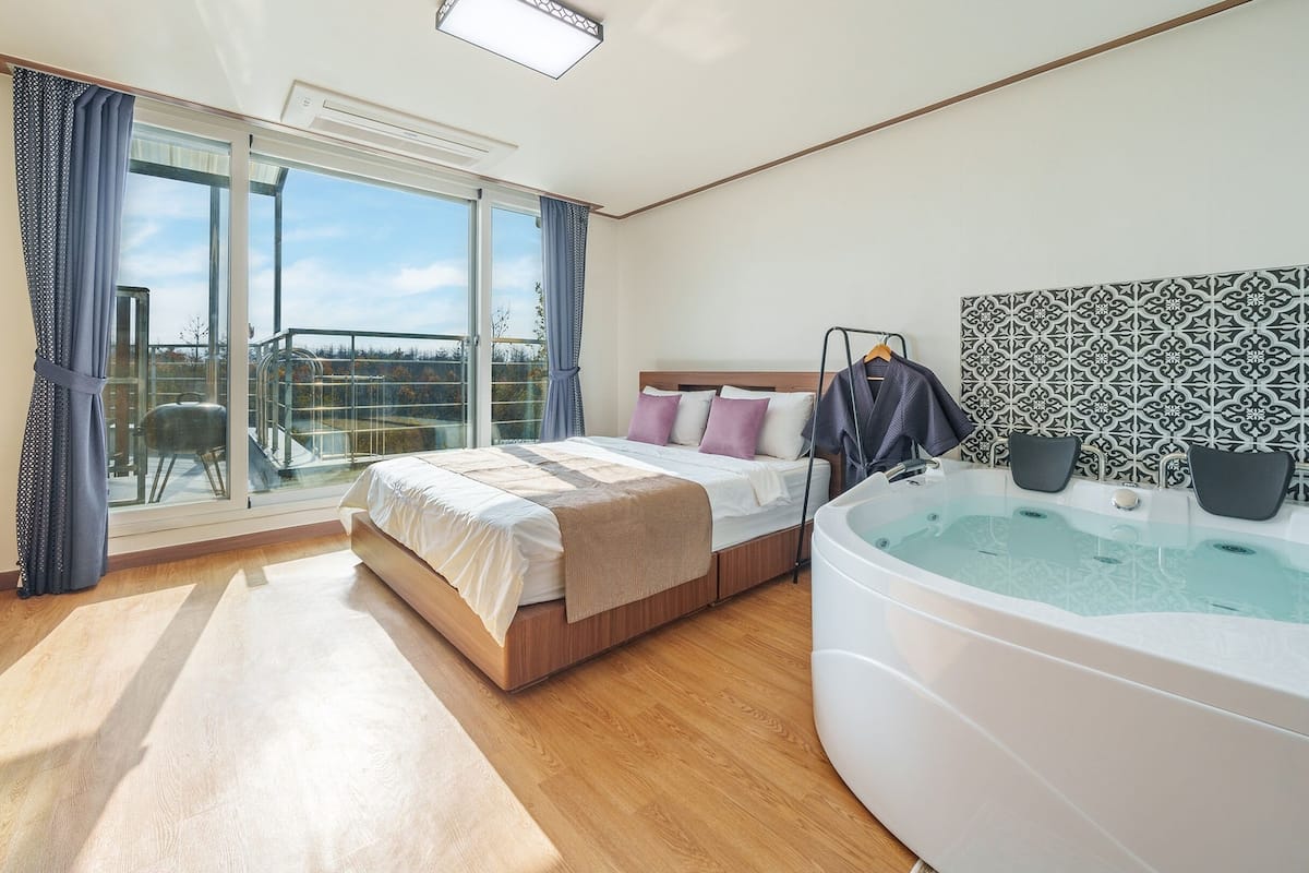 Een moderne hotelkamer met een groot bed, een eigen badkamer met whirlpool, een balkon met glazen deur en een televisie op een standaard.