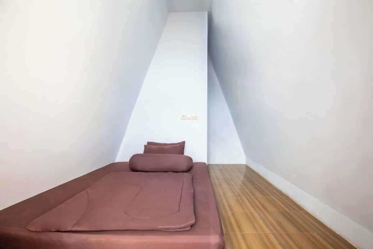 Une petite pièce avec un lit, un plancher en bois et un mur blanc.
