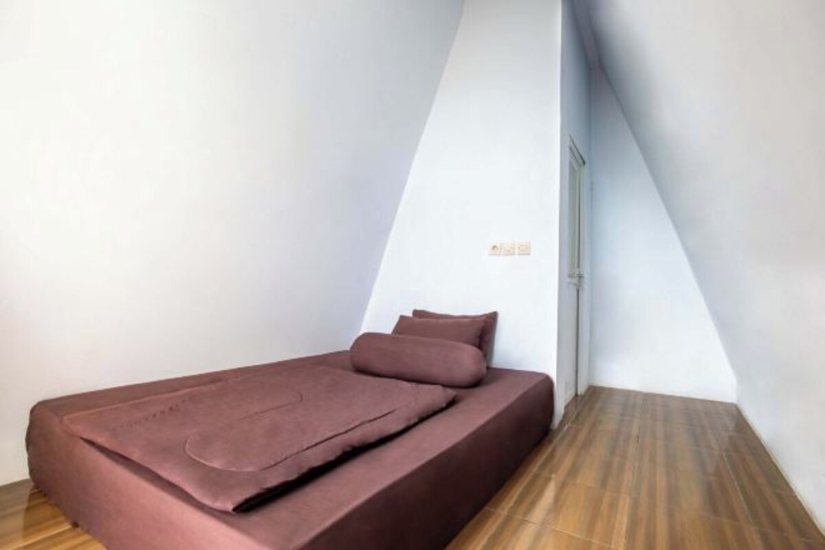 Une petite chambre avec un lit simple, un plafond en pente et un plancher en bois.