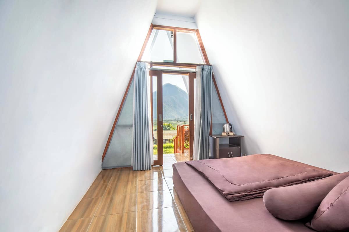 Une chambre avec un plancher en bois, un lit recouvert d’une couvre-lit rose, une fenêtre avec des rideaux et une vue sur une montagne.