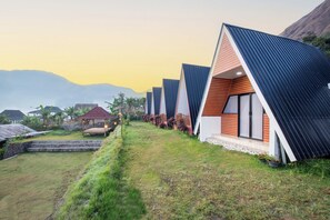 A row of modern, triangular-roofed cabins with a grassy pathway leading to them, set against a mountainous backdrop. - INKA Villas Sembalun (Sembalun Lawang)