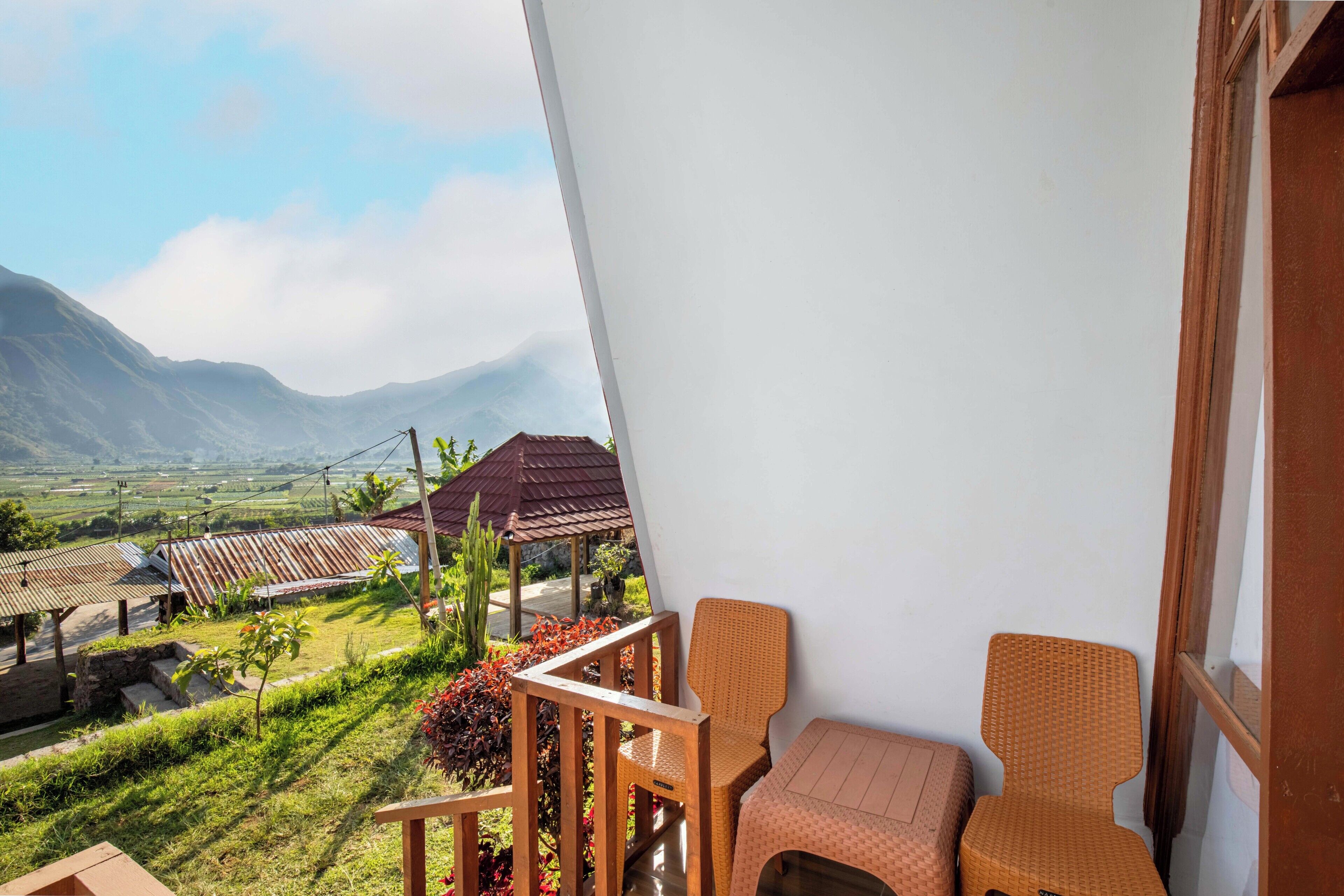 Un balcone con mobili in vimini, vista su un paesaggio rurale e una montagna sullo sfondo.