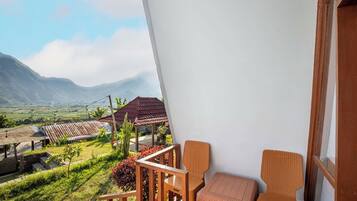 Een balkon met rieten meubilair, uitzicht op een landelijk landschap en een berg op de achtergrond.