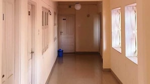 A hallway with a tiled floor, white walls, and a hanging light fixture. - The Grand Pratap (Dwarka)
