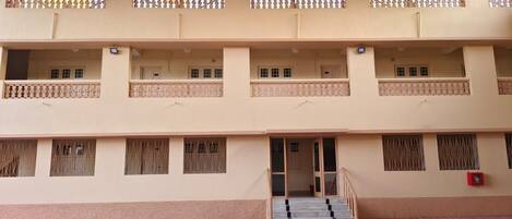 A multi-story building with balconies, windows with metal bars, and a staircase leading to the entrance.