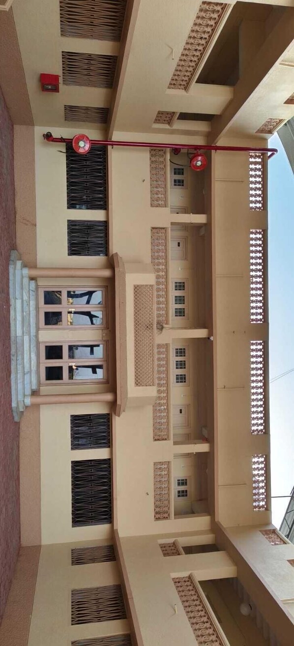 Un edificio a più piani con un cortile centrale, balconi con ringhiere decorate e una ventola rossa al secondo piano.