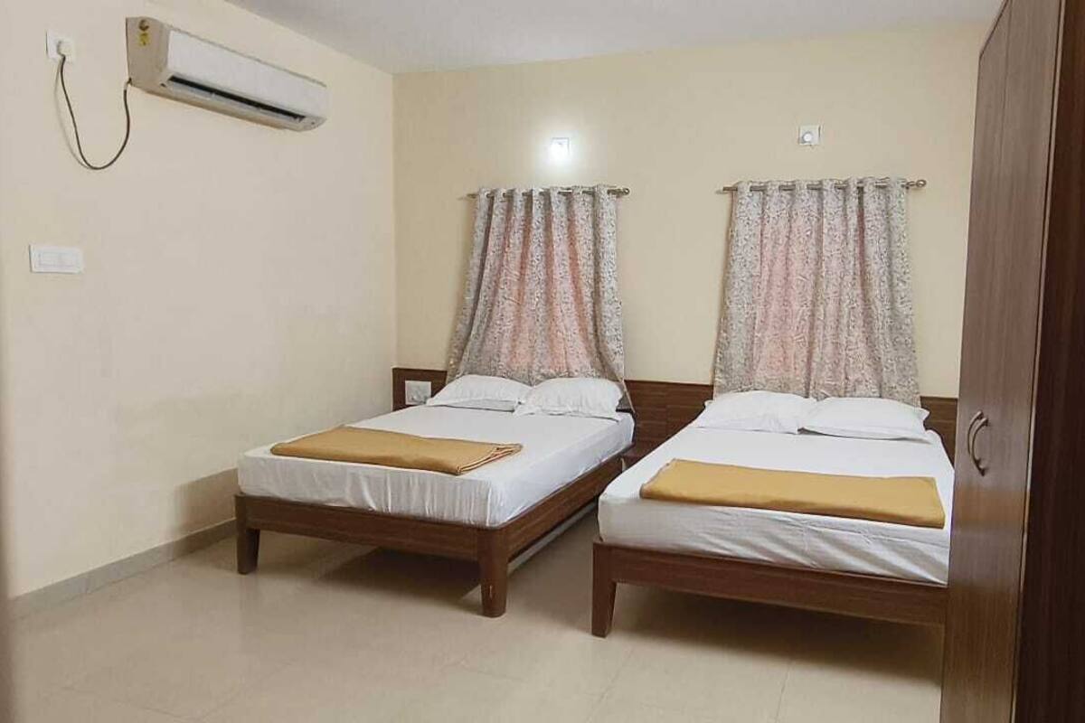 Une chambre avec deux lits simples, une armoire en bois, un appareil de climatisation et un rideau.