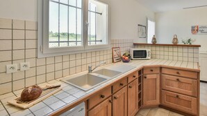 Una cocina con un lavamanos doble, armarios de madera, un microondas y un ventanal con vistas a un jardín.