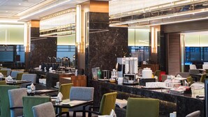 Un moderno vestíbulo de hotel con mostradores de mármol, sillones tapizados en verde y una estación de café.