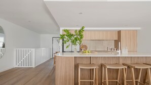 A modern kitchen with a white countertop, wooden bar stools, and a potted plant. - The Bowen Huskisson (Huskisson)