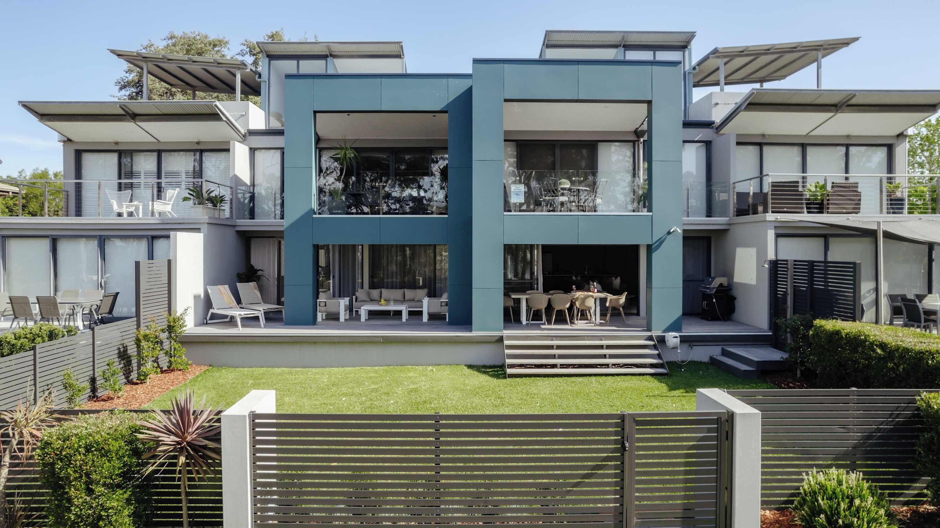 A modern two-story house with a flat roof, large windows, and a well-maintained lawn.