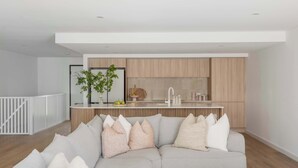A modern living room with a grey sectional sofa, a white coffee table, and a kitchen area with wooden cabinets and a white countertop. - The Bowen Huskisson (Huskisson)