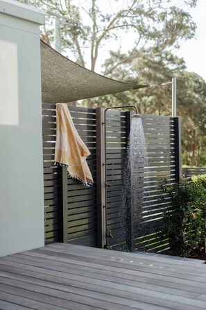 A modern outdoor shower area with a water feature, a towel hanging on a metal rack, and a wooden deck.