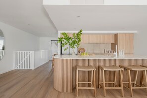 A modern kitchen with a white countertop, wooden bar stools, and a potted plant.