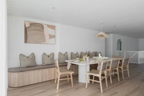 A modern dining area with a round table, wooden chairs, a bench with cushions, and a minimalist wall art piece. - The Bowen Huskisson (Huskisson)